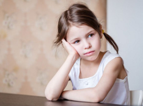 Печальная девочка сидит за столом