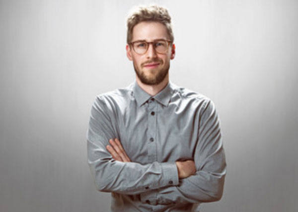 Мужчина стоит, скрестив руки перед собой. На его лице ухмылка