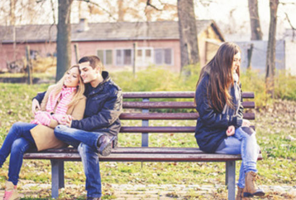 С одной стороны скамейки сидит парочка. На другом конце грустная девушка