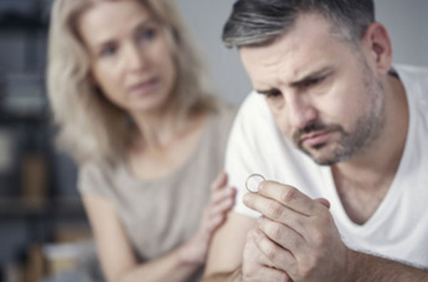 Мужчина держит кольцо в руке. Женщина сидит сзади него и держит за руку
