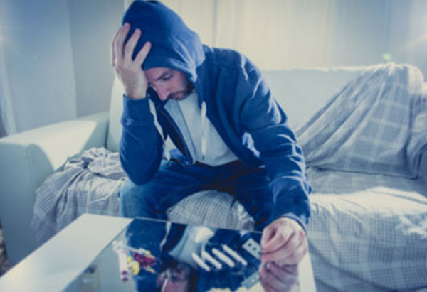 Мужчина держится за голову. На столике перед ним порошок