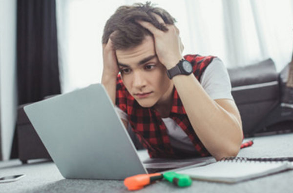 У парня растерянность в глазах. Он смотрит на экран ноутбука и держится за голову