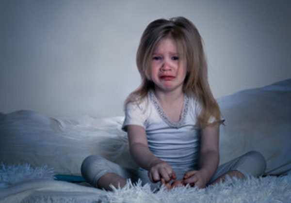 Заплаканная девочка сидит в темной комнате