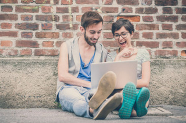 Веселые парень с девушкой сидят на асфальте, смотрят в ноутбук