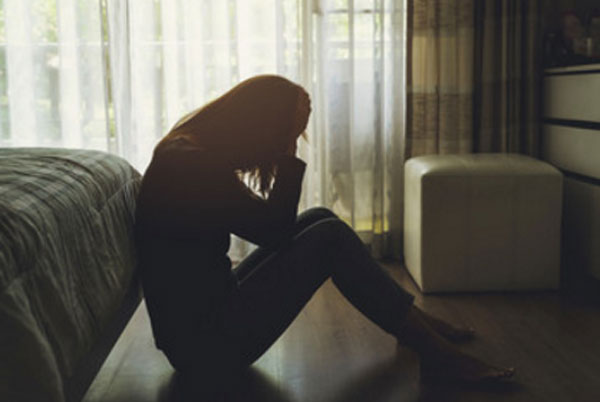 Женщина сидит на полу в темной комнате. У нее депрессия