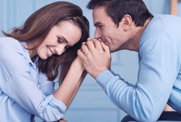 Муж с женой сидят друг напротив друга. Мужчина целует руки женщины, она смущается