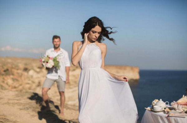 Парень с девушкой на вершине горы. Снизу море. У него букет цветов. Возле девушки накрытый стол. Барышня стоит спиной к парню