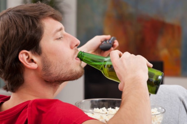 Мужчина с бутылкой пива и попкорном сидит перед телевизором