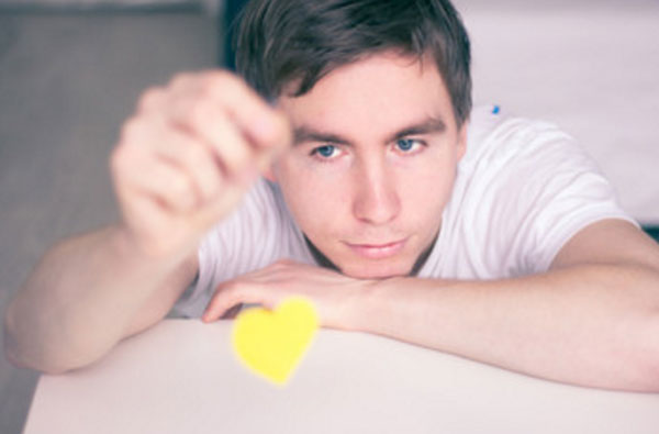 Задумчивый парень играет картонным сердечком