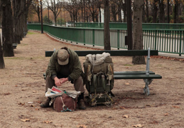 Мужчина сидит на скамейке. Перед ним сумка, рядом походный рюкзак