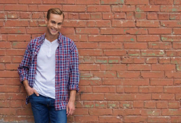 Одинокий улыбающийся мужчина стоит возле кирпичной стены