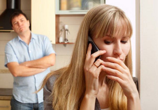 Женщина говорит по телефону, прикрываясь рукой. Мужчина стоит сзади. Начинает нервничать