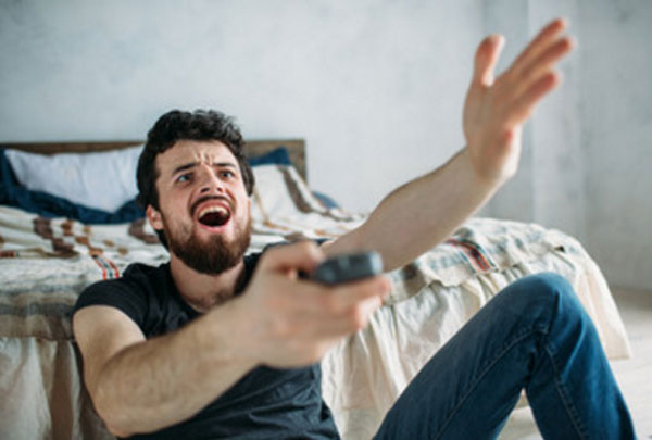 Мужчина сидит на полу с пультом в руках. Он недоволен чем-то происходящем на экране