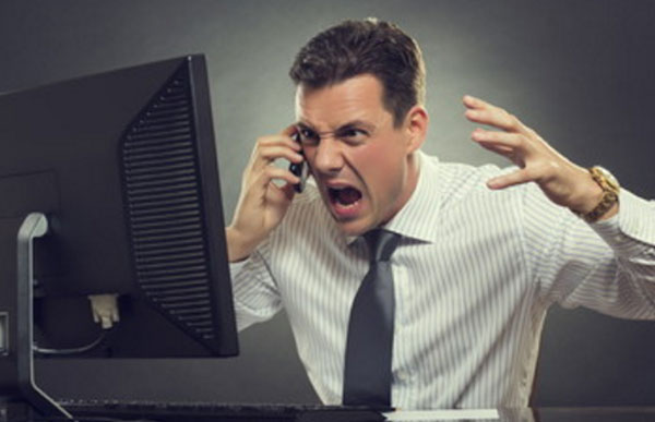 мужчина сидит за компьютером, в руках у него телефон. Он эмоционально общается