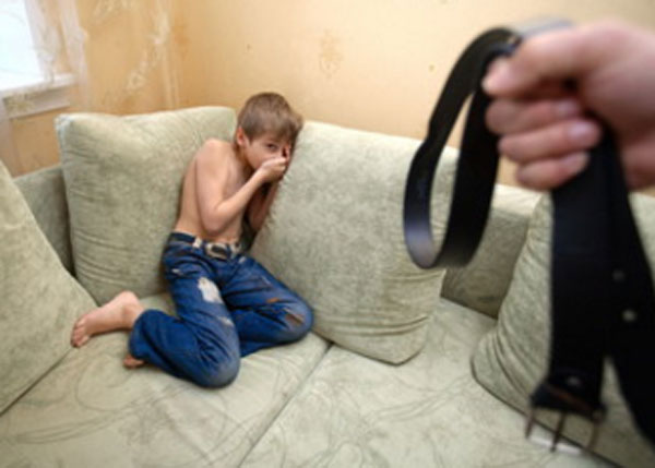 Перепуганный мальчик забился в угол дивана. К нему приближается рука с ремнем