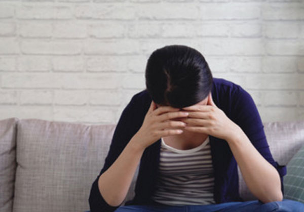 Женщина сидит с опущенной вниз головой, руками держится за лицо