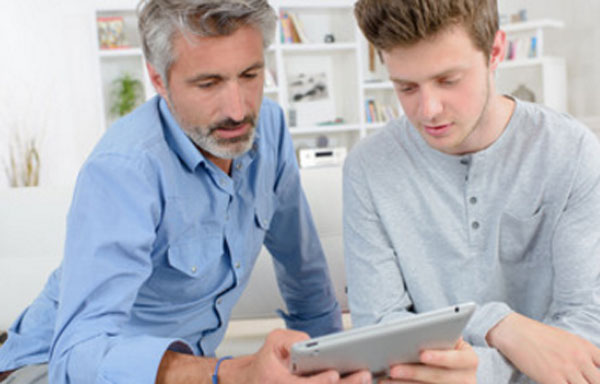 Отец что-то показывает юноше на планшете