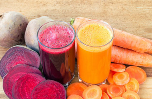 Два стакана с буряковым и свекольным соками. Рядом свекла и морковь, целые овощи и нарезанные кусочки