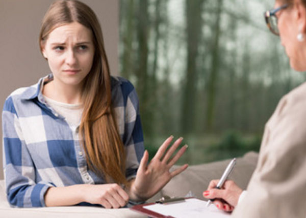 Сомневающаяся девушка. Перед ней сидит женщина в очках и хочет что-то написать