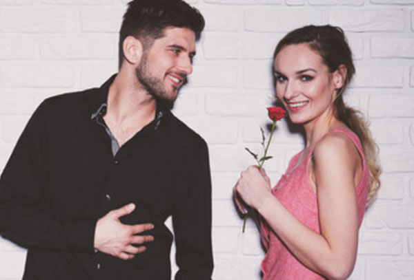 Парень смотрит на девушку влюбленными глазами. Она улыбается и держит в руке розу