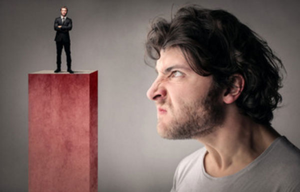 Мужчина агреесивно смотрит на маленького человека в костюме, стоящего на пьедестале