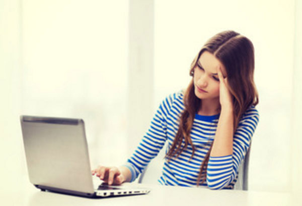 Грустная девушка сидит перед ноутбуком, что-то на нем смотрит