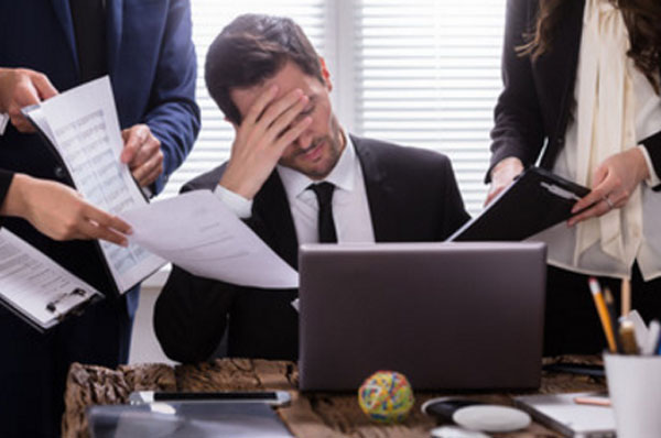 Замученный мужчина сидит перед ноутбуком. Его окружили люди, которые что-то от него хотят