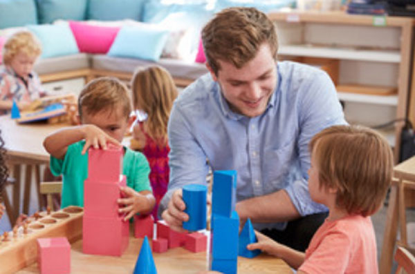 Мужчина сидит возле детей, которые строят башни из кубиков