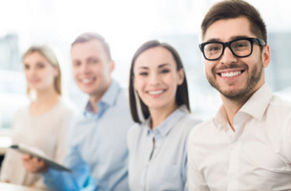 Четыре сотрудника сидят рядом, смотрят в камеру и улыбаются