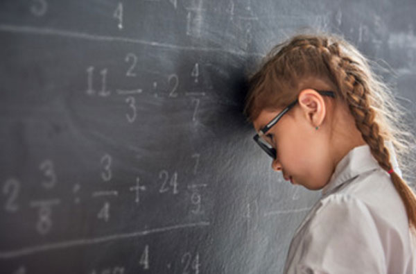 Девочка стоит у доски с примерами, лбом прислоняется к ней