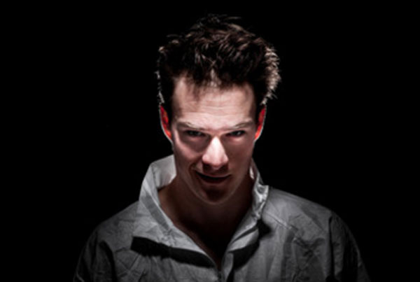 Мужчина с потрепанными волосами выглядывает из темноты и смотрит с ухмылкой