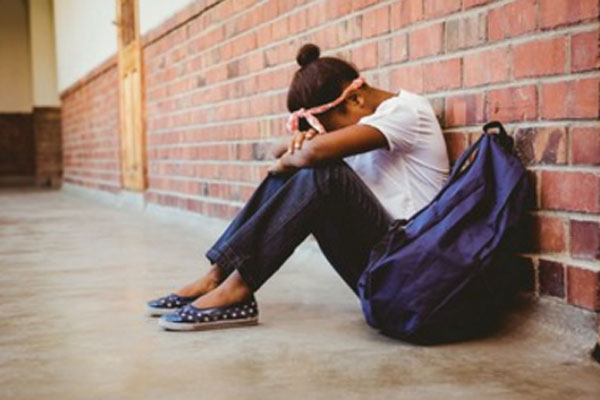 Расстроенная девочка сидит на полу. Рядом с ней школьный рюкзак