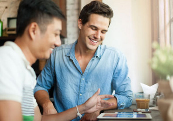 Два друга общаются. Один другому что-то показывает на планшете