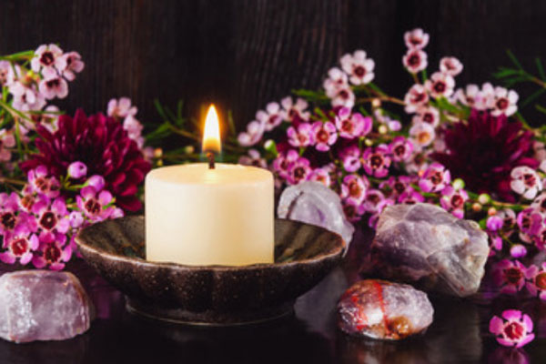 Зажженная свеча в мисочке. Рядом лежат камушки и стоят цветы