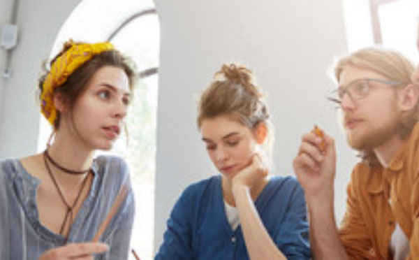 Парень с девушкой что-то обсуждают. Между ними сидит еще одна девушка, на лице которой полное безразличие