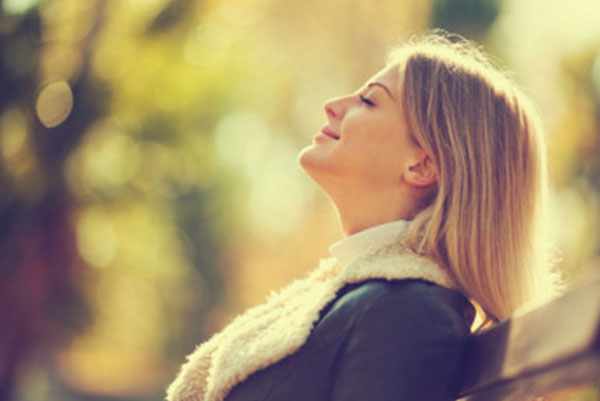 Счастливая женщина сидит в парке на скамейке, греется под лучами солнца