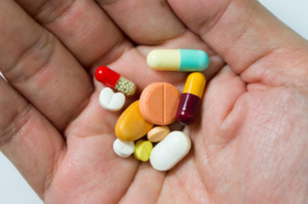 Рука человека, на которой лежат разные по форме, размеру и цвету таблетки и капсулы