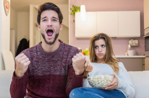 Пара сидит на диване. Девушка сидит с попкорном. парень в восторге, чему-то сильно радуется