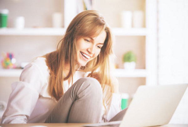 Девушка смотрит на экран ноутбука и смеется