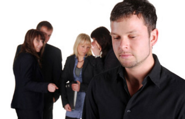 Мужчина стоит в сторонке. Сзади него собрались люди и о чем-то говорят