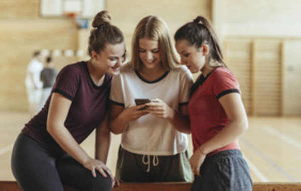 Девочка показывает подругам что-то на телефоне, пока они в спортзале