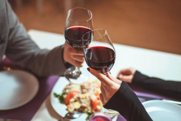 Пара сидит за столом, супруги подняли бокалы с вином