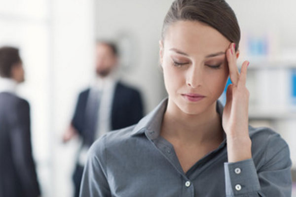 Женщина с закрытыми глазами держится за висок