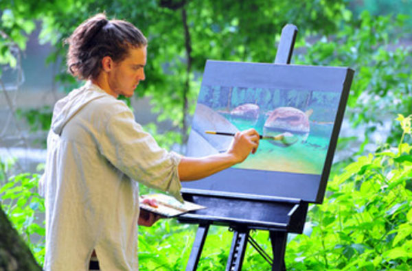 Парень рисует картину на природе