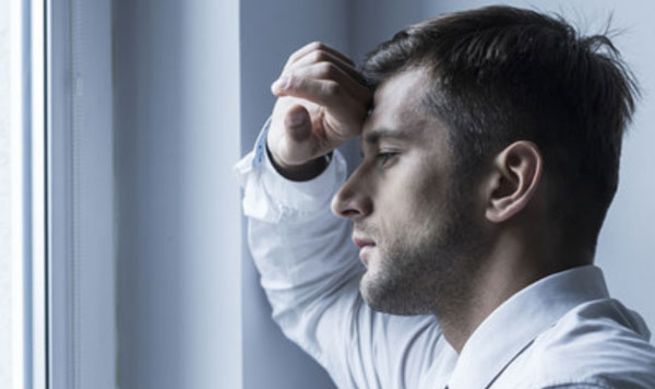Замученный мужчина стоит возле окна