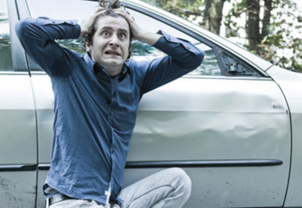 Мужчина в шоке, держится за голову. Сидит рядом со своей машиной, у которой разбито крыло