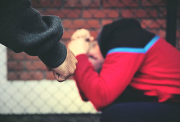 Парень сидит, прячет голову. К нему приближается человек со сжатым кулаком