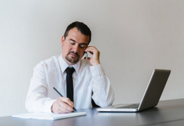 Мужчина работает. Перед ним ноутбук. Он что-то пишет и звонит по телефону