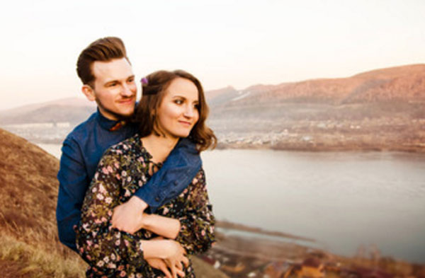 Парень стоит за спиной девушки и обнимает ее. Они стоят на возвышенности