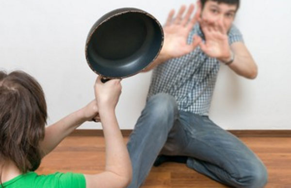 Перепуганный мужчина на полу. К нему подходит женщина со сковородой в руках